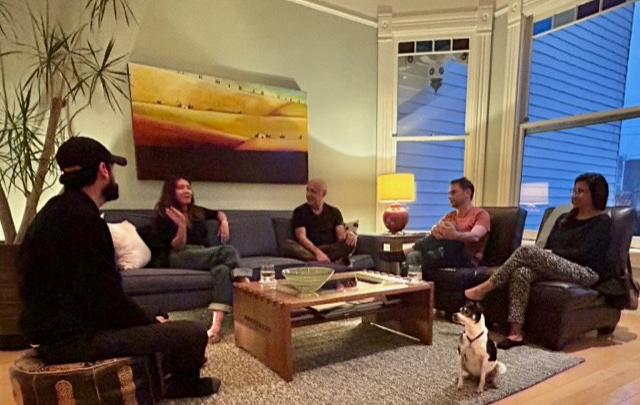 Five volunteers are gathered in a living room talking with a small dog keeping them company.